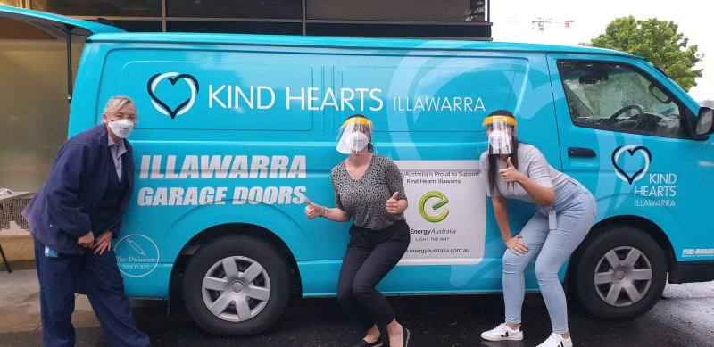 Three workers pose with thumbs up in front of an outreach van wearing protective gear