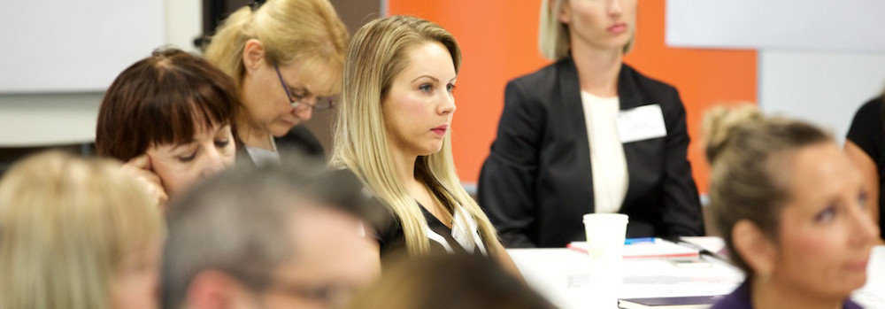 People sitting at desks in a conference room looking towards a speaker who is out of shot