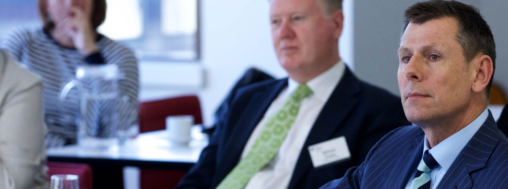 Two men sit while looking at a speaker out of shot