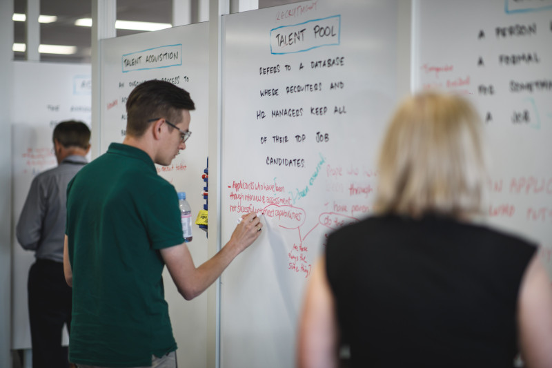 A man writes on a whiteboard under the heading Talent Pools