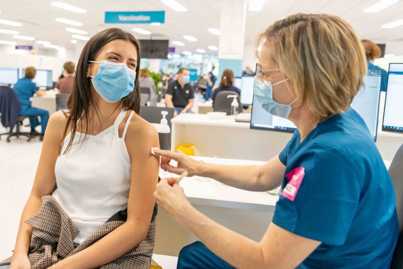 A woman in a face mask receives a vaccine from a female health worker