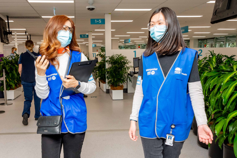 Two female vaccine centre workers walking together wearing blue vests