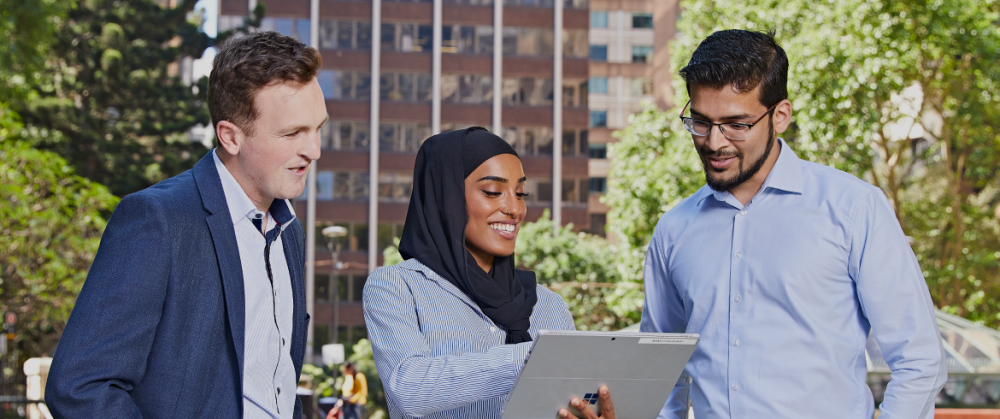 3 graduates stand together looking at a computer tablet