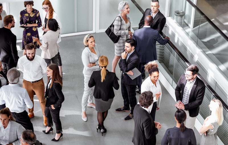 A large group stands talking in smaller groups in an open space