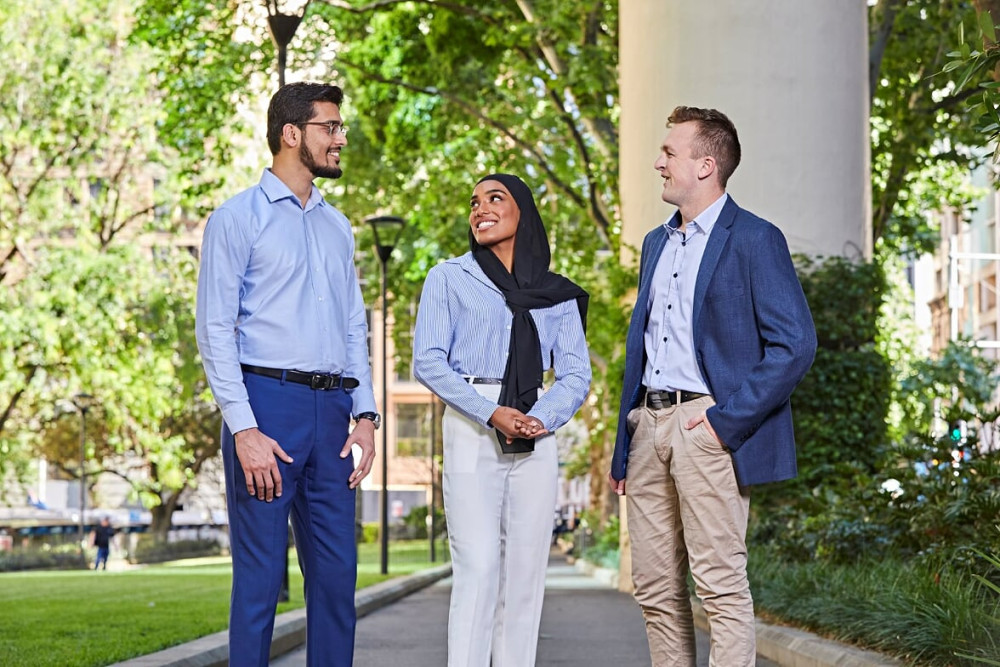 Three graduates (male, female, male) standing outside talking to each other