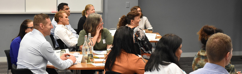 A group sit at desks looking to a speaker out of shot