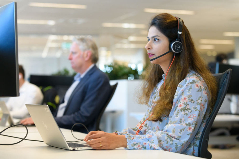 A woman works in an office with a headset on looking at a monitor