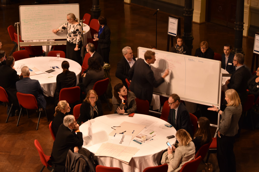 An overhead shot of a conference room with people sitting at tables and standing at whiteboards working together