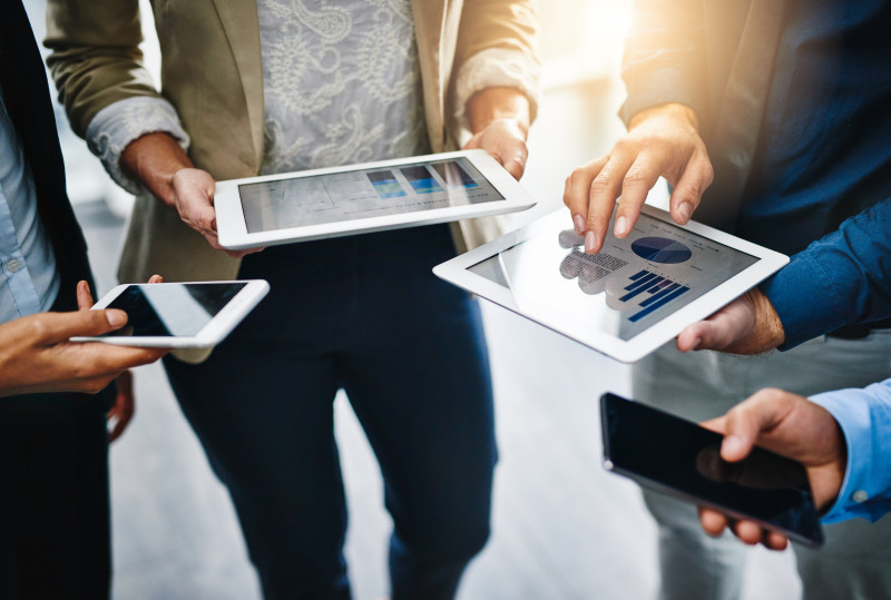 A group stand together looking at their tablets and mobile phones