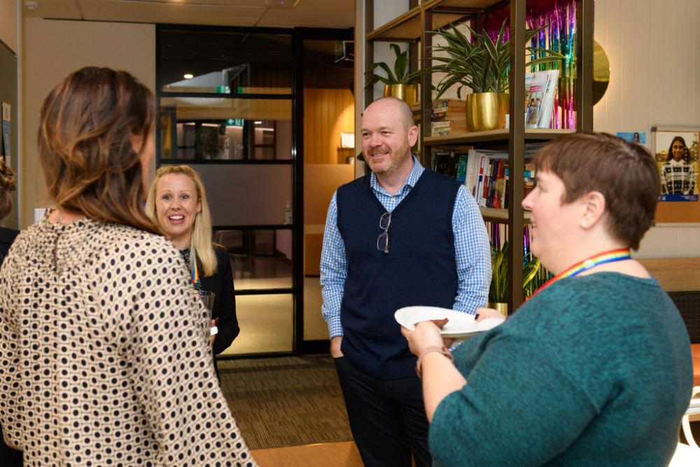 A group of 4 people stand in an office kitchen smiling in conversation with each other