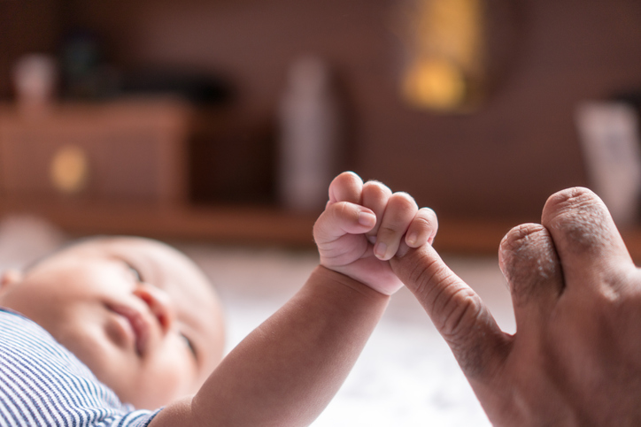 Baby lying down with arm out gripping dad's finger