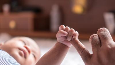 Baby lying down with arm out gripping dad's finger